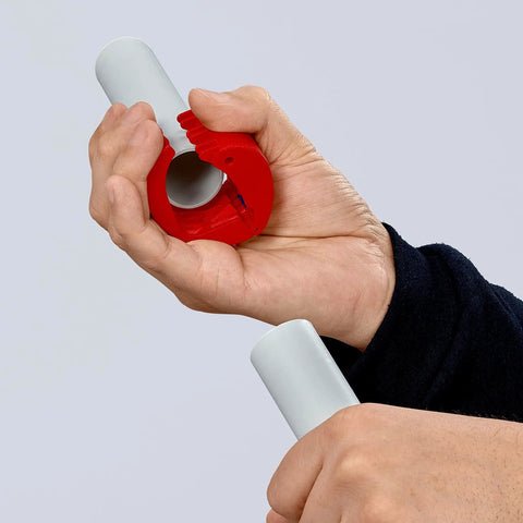 Hand using Pipe Cutter For Plastic Pipes 20 To 50 mm That Cuts Without Shavings, Ergonomic Handle, cutting a white plastic pipe.