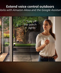 Woman using voice control near patio for Econic Up Outdoor Smart Wall Light Black With E26 Base White And Color Ambiance LED Bulb
