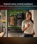 Person using voice control for Econic Square Outdoor Smart Wall Light, standing at glass door holding drink.