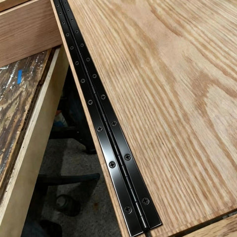 Heavy Duty Top Shelf Black Piano Hinge 48 Inches X 3 Inches Wide Stainless Steel Continuous Gate Door Hardware Tough Finish Cut To Size Quick Install installed on wooden surface showing screws.