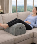 Carepeutic Contoured Leg Rest Wedge With Vibration Massage And Heat on a couch, grey soft surface, woman relaxing with elevated legs.