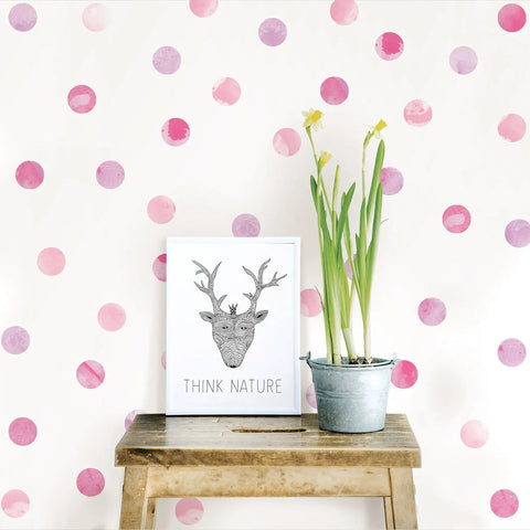 Pink Watercolor Dots Wall Art Kit Peel And Stick Repositionable Decor Set with 59 pieces displayed with plant on bench