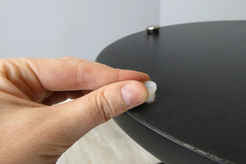 Hand inserting a round floor protector into a black table, showcasing Beat The Wobble Instantly 1 1/4 Inch Round Floor Protectors With Easy Twist Screw Threads To Stabilize Tables And Chairs Heavy Duty Silver Furniture Leveling Glides Set Of Four For Home Use.