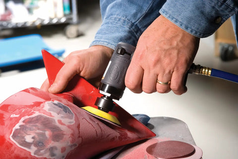 Person using compact mini orbital sander for metal prep and rust removal feather edging smoothing welds on red surface