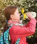 Girl drinking from Aviation Inspired 12oz Kids Water Bottle With Glider Silhouette Near A Red And White Wind Sock