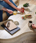 Marble coffee table with notebooks, glasses, drinks, salad, and sandwich with people reaching for beverages.