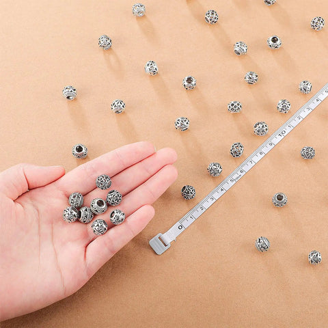 Hand displaying 60 Pieces Dope Silver Tone Filigree Spacer Beads Set Hollow Tibetan Alloy Beads In 10 Styles 10 Mm for DIY jewelry