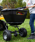 Person adjusting Deluxe Tow Behind Broadcast Spreader With Extended Easy Reach Handle And Weatherproof Cover, 175 lb capacity