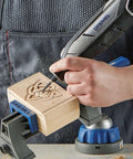 Side view of a Dremel 8240-5 cordless rotary tool carving a wooden block held in a blue bench vise.