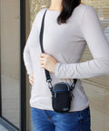 Person wearing Weatherproof Compact Camera Case With Padded Interior And Accessory Pockets, slim digital pouch, black.
