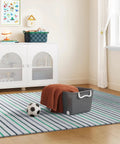 Smooth Rolling Storage Basket With Gray Plastic Mobile Organizer Bin Featuring Four Nifty Pivot Wheels Fold Down Handles For Easy Room To Room Moves Tailored For Keeping Laundry Clothes Toys And Closet Gear Tight And Square, placed on a striped rug with a soccer ball and folded blanket.