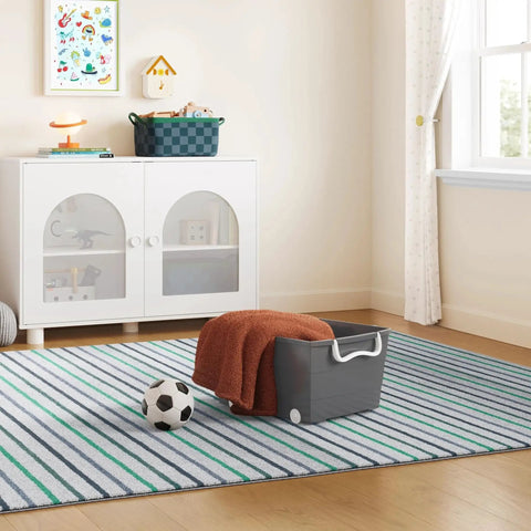 Smooth Rolling Storage Basket With Gray Plastic Mobile Organizer Bin Featuring Four Nifty Pivot Wheels Fold Down Handles For Easy Room To Room Moves Tailored For Keeping Laundry Clothes Toys And Closet Gear Tight And Square, placed on a striped rug with a soccer ball and folded blanket.