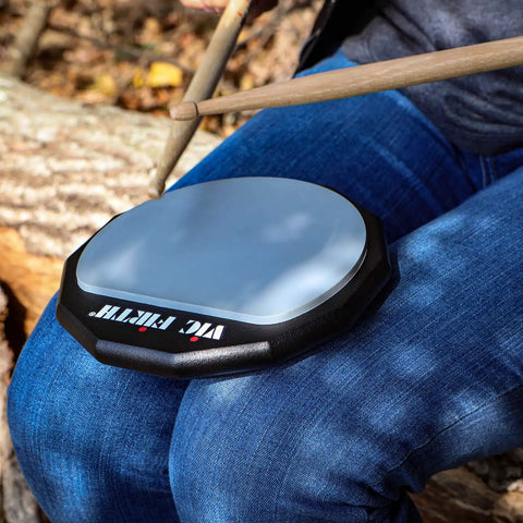 Six Inch Single Sided Practice Pad With Realistic Drumhead Feel And Low Volume For Quiet Jamming On The Go Natural Rubber On A Durable Wood Base To Train Wrists And Keep Your Chops Tight, shown on lap with drumsticks
