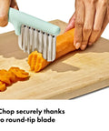 Oxo Tot crinkle cutter with mint-green handle and stainless steel blades slicing a carrot on a cutting board.