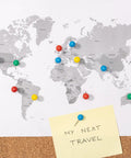 Colorful push pins on a world map with a note saying 'MY NEXT TRAVEL' on corkboard background.