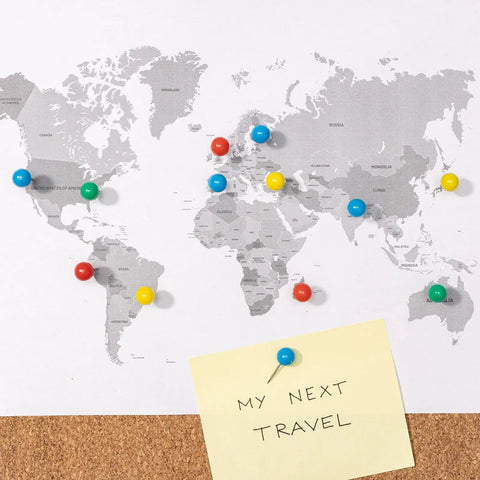 Colorful push pins on a world map with a note saying 'MY NEXT TRAVEL' on corkboard background.