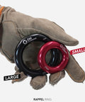 Gloved hand holding Black Large Rappel Ring 25kN for Rock Climbing Arborist Rescue Slackline Hammock Setup, side view