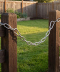 Stainless Steel Gate Chain Latch with Dual Carabiners for Fences securing a wooden fence post in a grassy yard.