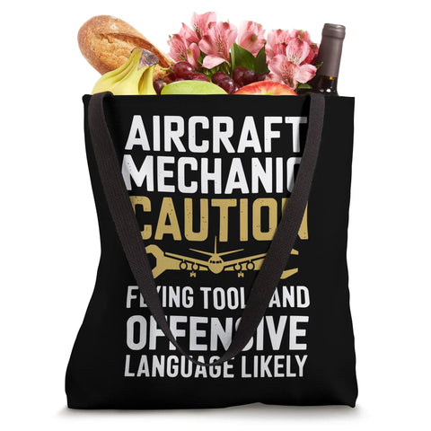 Caution Flying Tools Tote Bag For Aircraft Mechanic And Aviation Tech filled with flowers, wine, bread, and fruit.