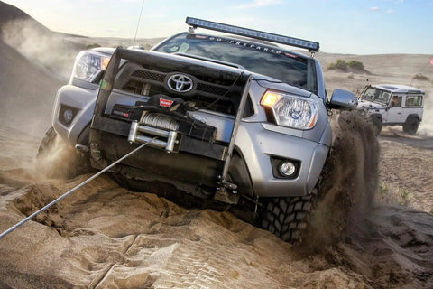 4x4 vehicle using winch to maneuver through sandy terrain with rugged tires visible, showcasing outdoor adventure capabilities.