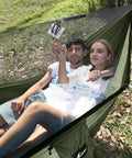 Couple relaxing in green Camping Hammock With Mosquito Net And Ridge Rope For Two, Extra Large 114x55 Inch, outdoors, tree straps visible