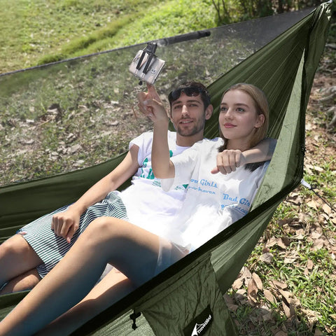 Couple relaxing in green Camping Hammock With Mosquito Net And Ridge Rope For Two, Extra Large 114x55 Inch, outdoors, tree straps visible