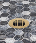 Universal 4 Inch Round Shower Strainer Snap In Bathroom Drain Cover Brushed Gold Stainless Steel installed on dark hexagonal tiles.
