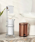 Freestanding Chrome Toilet Paper Roll Holder Stand That Fits All Roll Sizes Up To 5.5 Inches And Stores Up To Four Rolls At Once With No Drill And No Hardware Needed next to a white toilet and copper trash bin