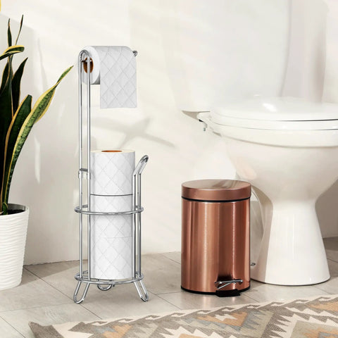 Freestanding Chrome Toilet Paper Roll Holder Stand That Fits All Roll Sizes Up To 5.5 Inches And Stores Up To Four Rolls At Once With No Drill And No Hardware Needed next to a white toilet and copper trash bin