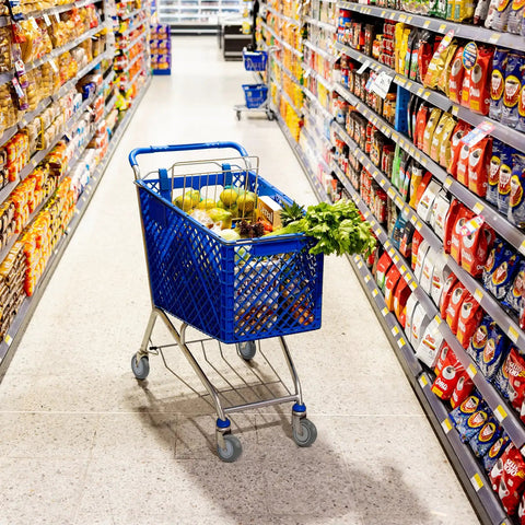 Blue shopping cart with groceries in a supermarket aisle, featuring lettuce, fruits, and cereal boxes.