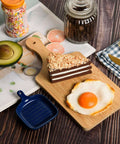 Front view of thick bamboo cutting board, 11x5 in; layered chocolate cake slice and fried egg on top.
