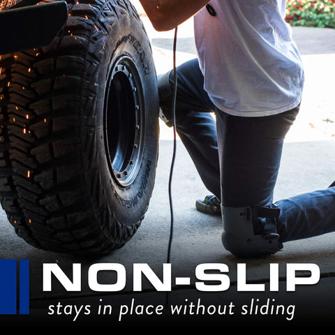 Person wearing All Day Comfort Knee Pads with Anti Slip Straps kneeling next to a tire, showcasing non-slip feature in outdoor setting.
