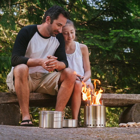 Father and daughter using Campfire 2 Pot Wood Burning Camping Stove Set For 4 Plus People Outdoor Kitchen Kit For Backpacking, Camping, And Survival With No Batteries Or Liquid Fuel Needed in forest.