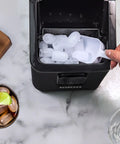 Igloo self-cleaning countertop ice maker, black, front view with white ice scoop and ice cubes.