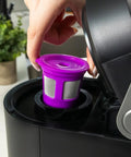 Placing purple reusable K-Cup filter into single cup brewer from Two Item Bundle With Reusable K Cup Coffee Filters Four Pack And EZ Scoop 2 Tbsp Scoop With Integrated Funnel Refillable Pod Capsules For Use With Most Single Cup Brewers Save Money On Every Brew.