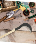 Long Handled Gardening Hand Scythe with Manganese Steel Blade on wooden table for weeding and cultivating, ergonomic tools around.