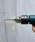 Masonry drill bit in a green cordless drill drilling into concrete wall with dust
