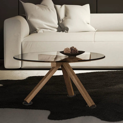 Glass-top coffee table with wooden legs on a black rug in front of a white sofa