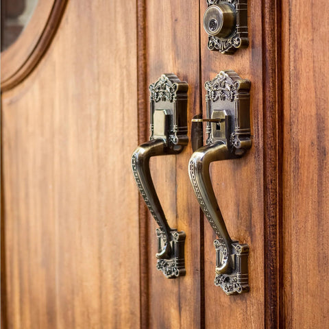 Front view of a pair of brass patina door handles with ornate backplates on a wooden door.
