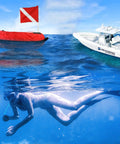 Inflatable Dive Float Buoy With Flag, 29 Inch Surface Marker For Scuba, Freediving, Snorkeling, And Spearfishing, High Viz Red And White Signal, Rugged Cordura Nylon Cover, Go To Training Safety Float near a diver and boat on the water.