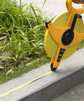 Heavy Duty Fiberglass Tape Measure 330 Feet 100 Meters Open Reel being used on rough site near grass and pavement