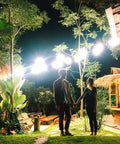 A couple holding hands under bright JUDYSSY Solar Flood Lights Outdoor Solar Flood Lights, illuminating a garden at night.