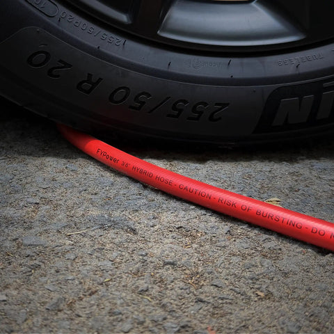 Reliable Workhorse Lightweight Hybrid Air Compressor Hose 3/8 Inch By 10 Feet under a car tire with caution label visible.