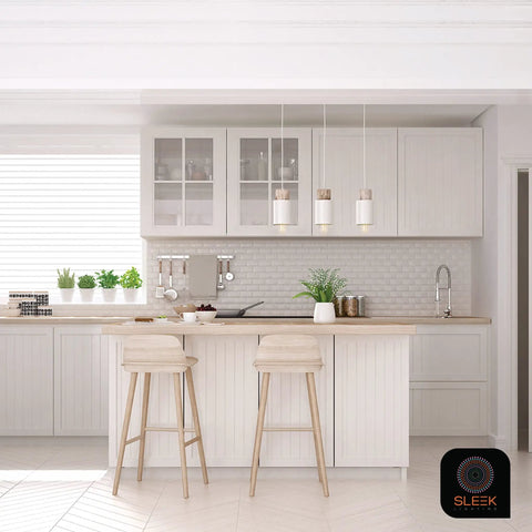 Modern kitchen with white cabinets, barstools, hanging lights, and potted plants on the countertop.