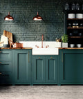 Modern kitchen with green cabinets and copper accents, featuring farmhouse sink and wooden countertop, under copper pendant lights.