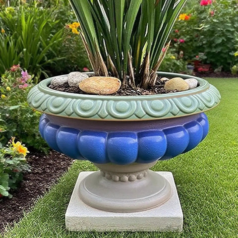 Large decorative garden planter with blue and green ornate design on a pedestal, filled with greenery, placed on grass.