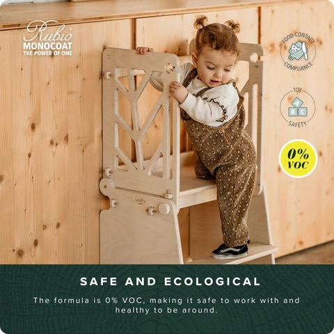 Child standing on wooden safety stool near cabinet with Go-To Wood Finish Safe Cleaning Soap For Floors, Furniture, And Cabinets label.