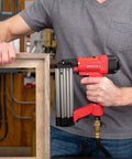 Worker using Oil Free 18 Gauge Pneumatic Brad Nailer For Small Trim And Interior Molding Fires Up To 100 PSI Handles Five Eighths To Two Inch Brad Nails Tool Free Jam Release Easy Load Magazine Quiet Exhaust The Go To Finish Work Buddy on wooden frame in workshop
