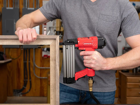 Worker using Oil Free 18 Gauge Pneumatic Brad Nailer For Small Trim And Interior Molding Fires Up To 100 PSI Handles Five Eighths To Two Inch Brad Nails Tool Free Jam Release Easy Load Magazine Quiet Exhaust The Go To Finish Work Buddy on wooden frame in workshop
