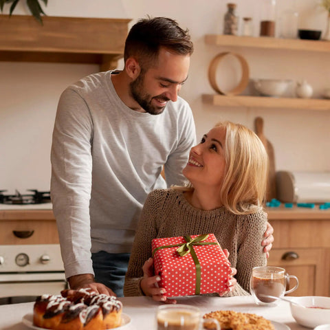 Couple in a kitchen exchanging a gift with pastries and coffee on the table